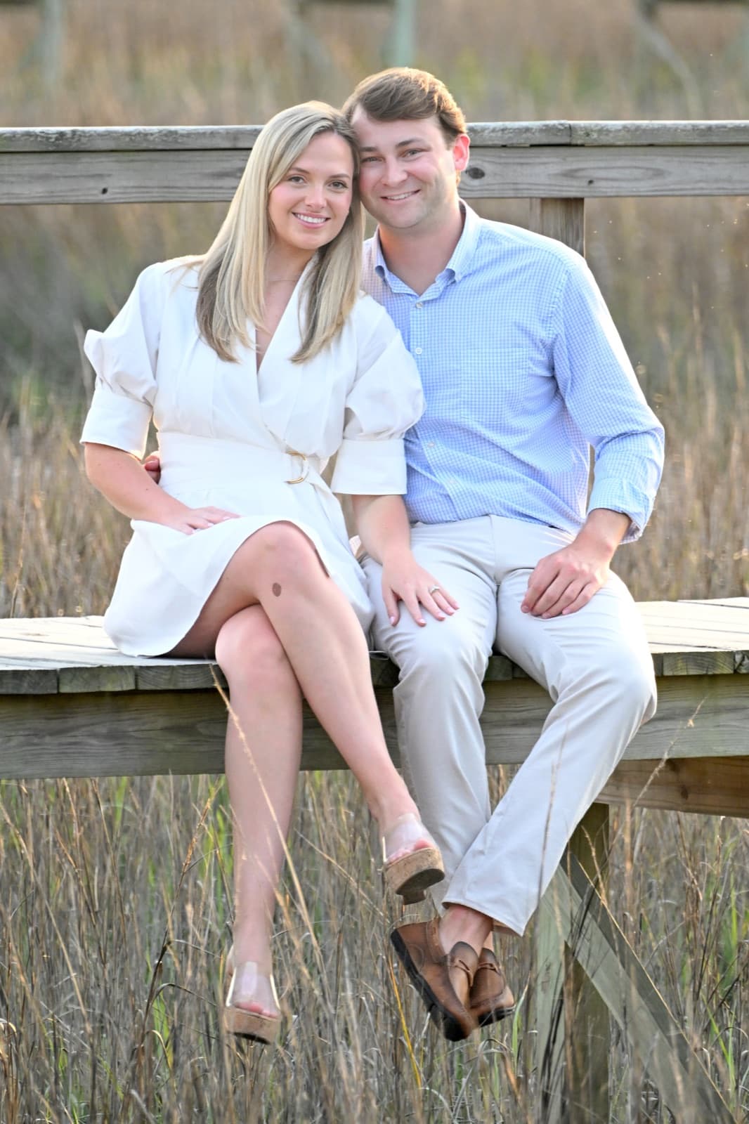 Allie and Chris sitting together on a boardwalk at golden hour